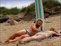 The babe in blue bikini is lying on the beach and having her back being spread with a tanner!